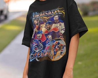 May include: A black short-sleeve t-shirt featuring a graphic print of hockey player Leon Draisaitl in various action poses. The design includes yellow lightning bolts, the text "DRAISAITL" in bold letters, and "Leon" in a cursive script font.