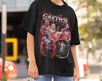 May include: A black short-sleeve t-shirt featuring a graphic print of mixed martial artist Justin Gaethje. The design includes multiple action photos of the fighter, red lightning effects, and the text "Justin Gaethje The Highlight" in white.