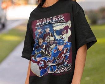 May include: Black t-shirt featuring a vintage-style graphic of hockey players, including Cale Makar, holding a trophy. The graphic includes the text "Makar" and "Cale".