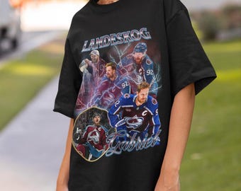 May include: Black t-shirt with a graphic of hockey players, the name "LANDESKOG" at the top, and "Gabriel" in a stylized font. The design features players in team uniforms with lightning bolt accents. A sports-themed garment.