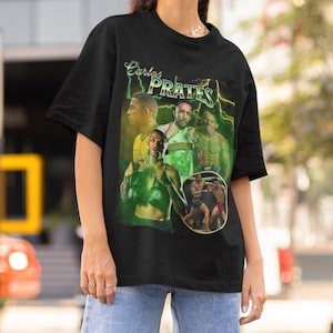 May include: Black t-shirt featuring a graphic design with the name "Carlos PRATES" in green and yellow. The design includes images of athletes in action, with a green and yellow color scheme. The shirt is made of a soft material.