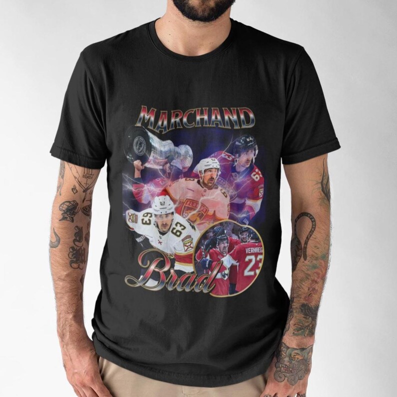以下が含まれることがあります： 黒いTシャツ。ヴィンテージスタイルのグラフィックで、ホッケー選手「Marchand」と「Brad」の名前が装飾的なフォントで描かれています。デザインには、紫と赤の背景の中で、選手が活躍している様子が描かれています。