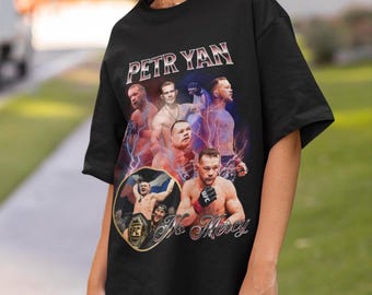 May include: A black short-sleeve t-shirt featuring a graphic print of mixed martial artist Petr Yan. The design includes multiple images of the fighter, purple lightning effects, the text PETR YAN at the top, and No Mercy at the bottom.