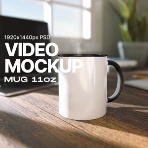 Puede incluir: Taza de cerámica blanca con borde y asa negros. La taza está sobre una mesa de madera con un portátil en el fondo. El texto "VIDEO MOCKUP MUG 11oz" está impreso en la taza.