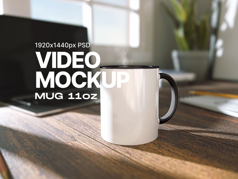 May include: White ceramic mug with a black rim and handle. The mug is sitting on a wooden table with a laptop in the background. The text "VIDEO MOCKUP MUG 11oz" is printed on the mug.