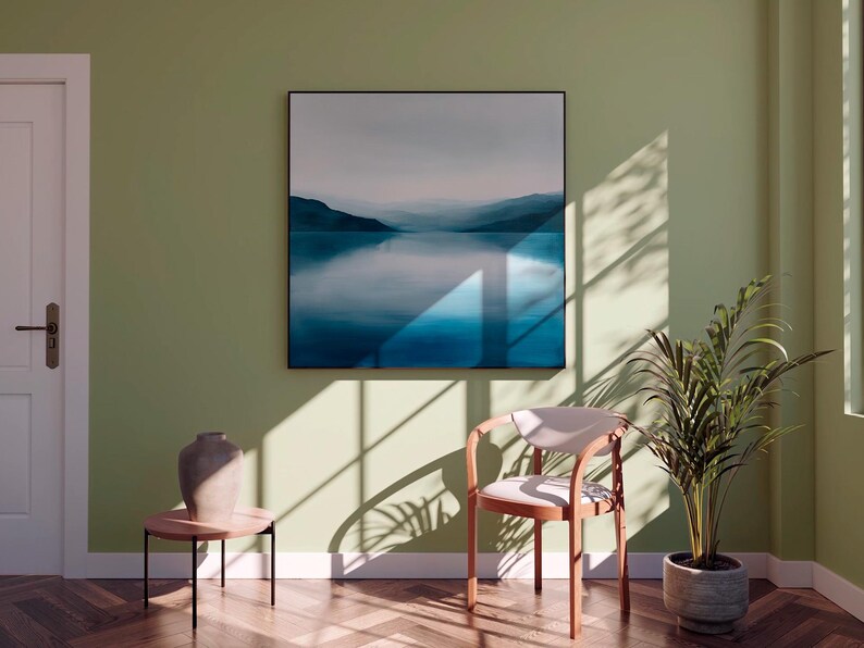 Peut inclure: Int&eacute;rieur serein avec une grande &oelig;uvre d'art encadr&eacute;e repr&eacute;sentant un paysage bleu et blanc. Une chaise moderne, une petite table d'appoint avec un vase et une plante en pot sont &eacute;galement pr&eacute;sents. La pi&egrave;ce est peinte dans une teinte verte douce.