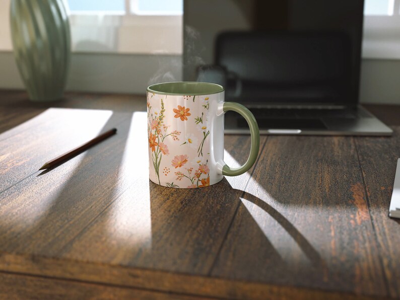 May include: A white ceramic mug with a floral pattern in shades of orange, pink, and green. The mug has a green rim and handle. Steam is rising from the mug, suggesting it is filled with a hot beverage.