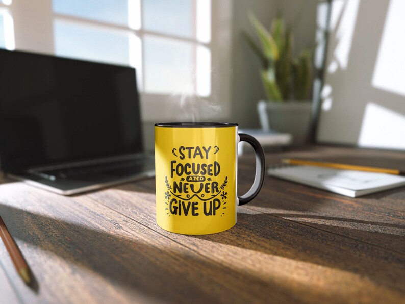 May include: Yellow coffee mug with a black rim and handle. The mug has black text that reads "Stay Focused and Never Give Up".