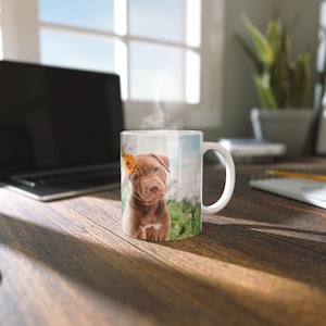 May include: A white ceramic mug with a brown puppy with a yellow flower behind its ear printed on it. The puppy is sitting in a grassy field.