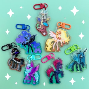May include: A collection of colorful acrylic keychains featuring various cartoon pony characters. Each keychain has a unique design with vibrant colors and attached with a metal clasp in different colors. The background is a light teal color with white star shapes.