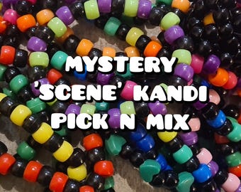 May include: A close-up of a variety of colorful kandi bracelets with black beads. The bracelets are arranged in a pile and the text "MYSTERY 'SCENE' KANDI PICK N MIX" is visible in the center of the image.
