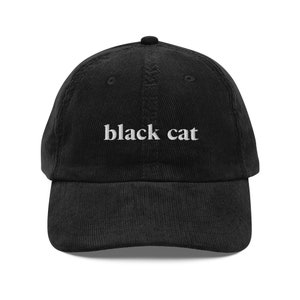 May include: A black corduroy baseball cap with white embroidered text that reads "black cat".