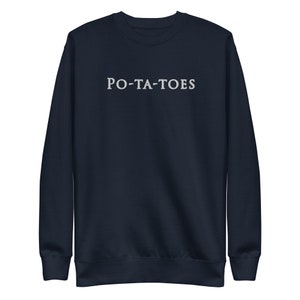 Op de afbeelding: Marineblauw sweatshirt met het woord "PO-TA-TOES" in het wit, gecentreerd op de borst. De top met lange mouwen en ronde hals is gemaakt van een zacht materiaal.