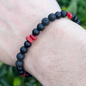 Peut inclure: Bracelet composé de pierres de lave noires et de perles noires mates, avec des touches de corail rouge. Les perles mesurent environ 8 mm de diamètre. Un accessoire élégant pour un usage quotidien.