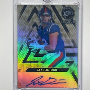 Könnte beinhalten: Eine Jaxon Dart Football-Sammelkarte in einer Schutzhülle. Die Karte zeigt einen Spieler in blauem Trikot mit einem Football und einem holografischen Hintergrund. Die Karte ist mit "JAXSON DART" beschriftet und enthält ein Autogramm.