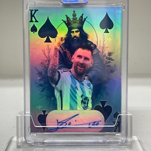 Könnte beinhalten: Eine Spielkarte mit einem Fußballspieler mit Krone und einem Pik-König-Design. Die Karte hat ein holografisches Finish und ist in einem transparenten Kunststoffhalter eingeschlossen. Die Karte wird auf einem transparenten Kunststoffständer ausgestellt.