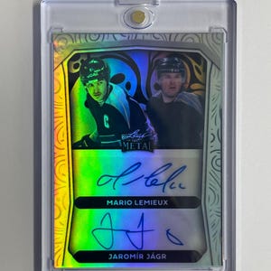 Puede incluir: Una tarjeta de hockey con autógrafos de Mario Lemieux y Jaromir Jagr. La tarjeta tiene un diseño holográfico con imágenes de los jugadores con sus uniformes de hockey. Está encapsulada en un soporte protector transparente.