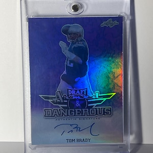 Puede incluir: Una tarjeta coleccionable de Tom Brady "Draft & Dangerous" en un estuche protector. La tarjeta presenta una imagen de Brady con su uniforme de f&uacute;tbol, con su firma debajo del texto. La tarjeta tiene un fondo hologr&aacute;fico.