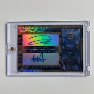 Può includere: Una carta sportiva a doppia firma racchiusa in un supporto di plastica trasparente. La carta presenta due immagini di giocatori e due autografi. La carta ha il testo "Multi Graphics LEAF" e "DUAL GRAPHICS".