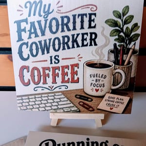 May include: A square decorative sign featuring the text My Favorite Coworker Is Coffee in blue and red. The image includes a coffee mug labeled Fueled By Focus, a small notepad with the text Good Plan, Strong Coffee, Crush It, a keyboard, and pens.
