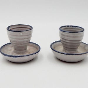 Puede incluir: Dos tazas de huevo de cerámica blanca con ribete azul, cada una sentada en un platillo a juego. Las tazas tienen un patrón de remolino.