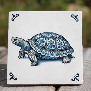 Könnte beinhalten: Eine blaue und weiße Keramikfliese mit einem dekorativen Design einer Schildkröte. Die Schildkröte geht nach rechts und hat einen detaillierten Panzer mit einem blauen und weißen Muster.