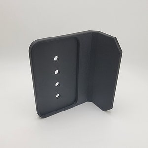 Könnte beinhalten: Schwarzer Telefonständer aus Kunststoff mit fünf Löchern für Ladekabel. Der Ständer hat eine rechteckige Basis und eine vertikale Seite.