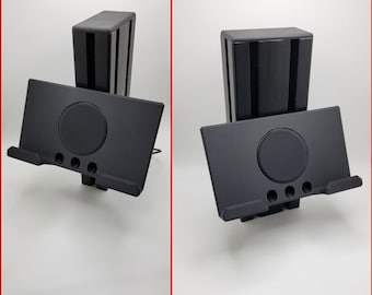 May include: A black plastic stand with a slot for a tablet or phone. The stand has a circular cutout in the center and a small lip on the front to hold the device in place.