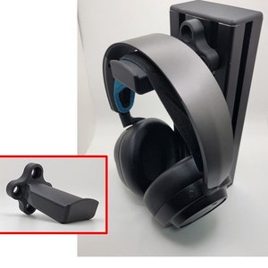 Puede incluir: Soporte de auriculares de plástico negro con auriculares grises colgados. El soporte tiene una pequeña perilla negra en el lateral. Los auriculares tienen un diseño azul y negro.