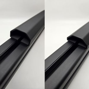 May include: Close-up of two black plastic covers for a metal track system. The covers are designed to fit over the track and protect it from damage.
