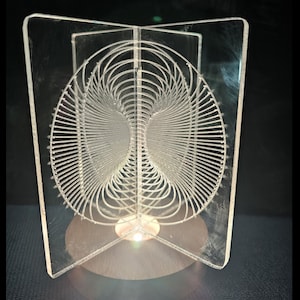 Puede incluir: Una escultura de acrílico transparente con un diseño geométrico, iluminada desde abajo por una pequeña fuente de luz. La escultura está sobre una base de madera.