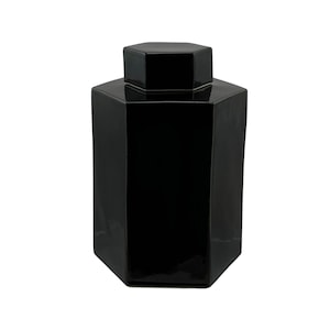Peut inclure: Un pot en céramique hexagonal noir avec un couvercle. Le pot a une finition lisse et brillante.