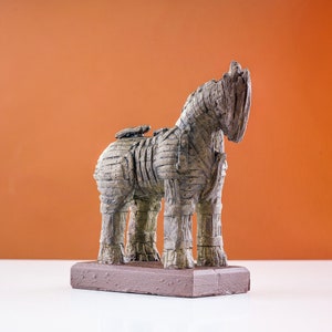 Marble dust Trojan Horse statue with a striated acrylic finish in charcoal and umber shades, on a terracotta backdrop for contrast