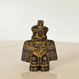 May include: A small, dark brown figurine with a crown-like headpiece and intricate yellow detailing. The figure has a stylized, blocky form with geometric patterns and a regal appearance. The overall design suggests an ancient or historical theme.