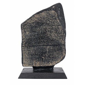 Puede incluir: Una escultura negra y rectangular que se asemeja a una tableta de piedra, montada sobre una base cuadrada. La tableta tiene una superficie texturizada con inscripciones visibles. La escultura es oscura con acentos más claros y envejecidos.