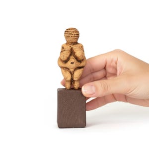 Handheld close-up of the Venus of Willendorf Statue by ArkeoArt, showing its detailed handmade surface and compact size in human hand for scale. This Paleolithic fertility goddess replica reflects prehistoric craftsmanship, divine femininity, and the spiritual origins of art. Ideal for collectors of ancient artifacts and goddess-inspired decor.