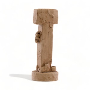 May include: A tall, brown, ceramic sculpture with a square top and a round base. The sculpture is decorated with carvings of animals and other designs.