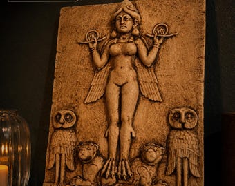 May include: A rectangular stone-colored wall plaque featuring a relief carving of a winged figure with a headdress, holding two rings. The figure stands atop two lions, flanked by two owls. The text Customer Display is visible in the top corner.