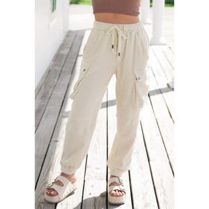 May include: Cream colored corduroy cargo pants with a drawstring waist and multiple pockets. The pants are cuffed at the ankles and are worn with white platform sandals.