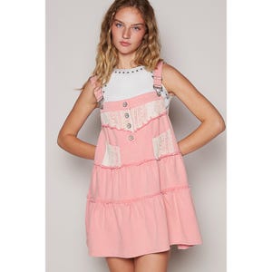 May include: A pink tiered denim overall dress with white lace detailing and silver button accents.