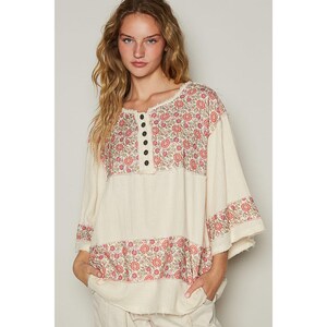 May include: A white, loose-fitting, 3/4 sleeve top with a floral print in shades of pink and green. The top has a button closure at the neckline and a relaxed fit.