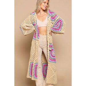 Peut inclure: Un long cardigan en crochet beige avec une capuche. Le cardigan présente des motifs circulaires colorés dans des tons de rose, violet et vert.
