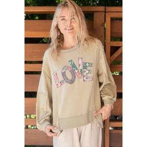 May include: A light green sweatshirt with a distressed look and a large "LOVE" graphic made of colourful patchwork fabric.