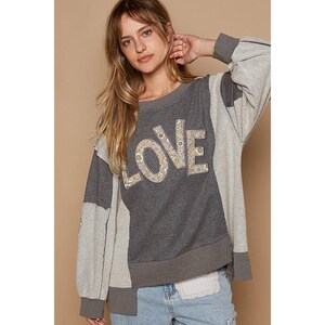 May include: A gray and white patchwork sweatshirt with the word "LOVE" embroidered in floral fabric on the front.