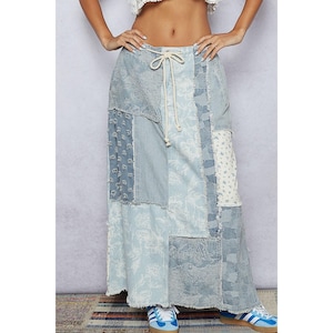 May include: A long, patchwork denim skirt in shades of light blue and white. The skirt features a drawstring waist and a variety of denim patterns, including floral and striped designs. The skirt is floor-length.
