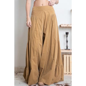 May include: Wide-leg, tiered pants in a light brown color. The pants have a high waist and a relaxed fit.