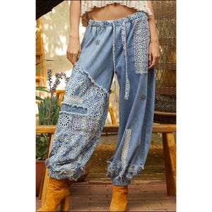 Könnte beinhalten: Hellblaue Jeanshose mit Patchwork-Details. Die Hose hat gestickte und Spitzen-Akzente, einen Kordelzug in der Taille und geraffte Knöchel. Das Design umfasst florale und geometrische Muster, die einen Boho-Look erzeugen.