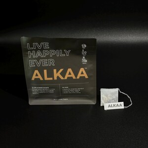 May include: A black pouch with the text "LIVE HAPPILY EVER ALKAA" in white and gold. A small tea bag with the word "ALKAA" is next to the pouch. The pouch contains 24 life altering sachets.