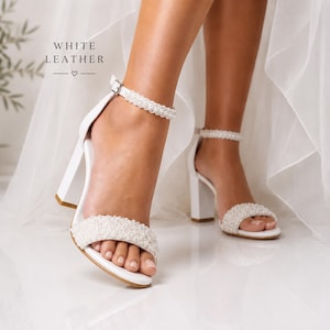 Close-up of white leather bridal sandals with pearl embellished straps, 8 cm block heels and handmade craftsmanship by YVOLLA.