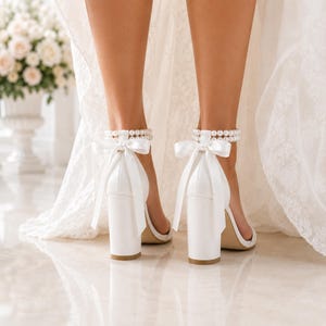 Back view of white bridal heels showing double pearl ankle straps, ribbon bows and block heels.